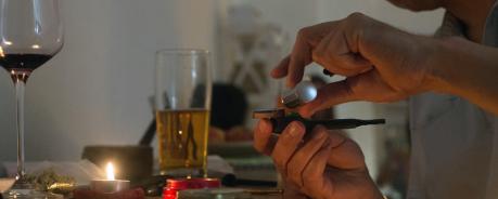 Mischkonsum von Drogen, Wechselwirkungen, Risiken und Schutz Zwei Hände befüllen eine Pfeife, im Hintergrund mehrere Gläser Alkohol, eine Pillendose und ein Tütchen